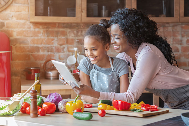 Mom and daughter read recipe on tablet while cooking