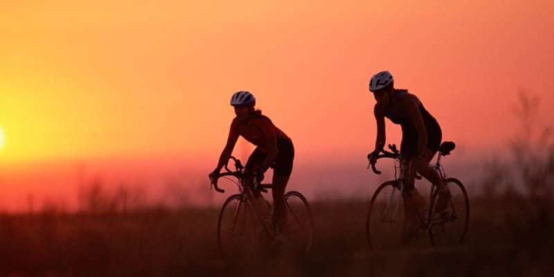 Two bicyclists riding at sunset.
